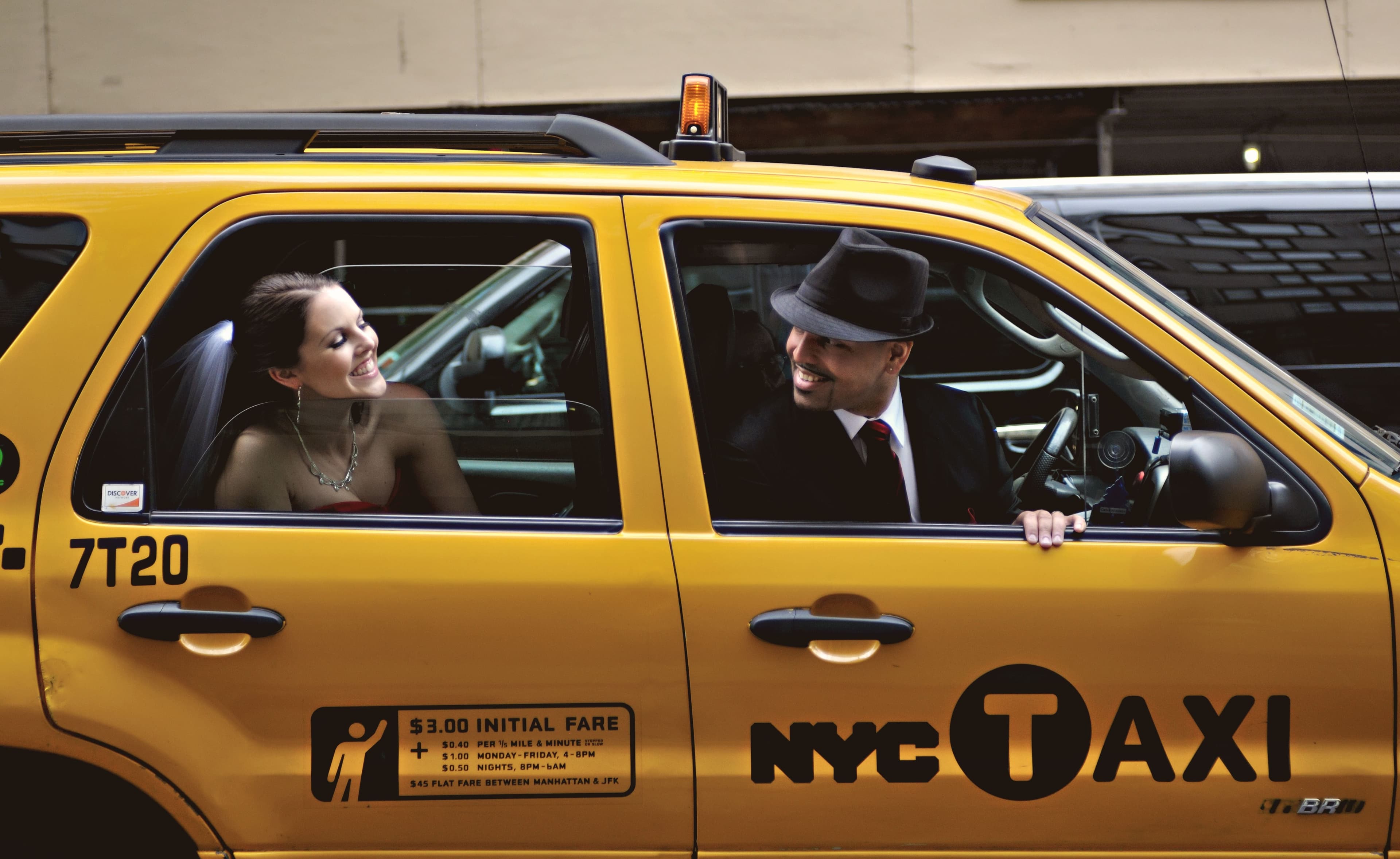 A bride and a groom in a fedora smile at each other through the windows of a yellow New York City taxi.